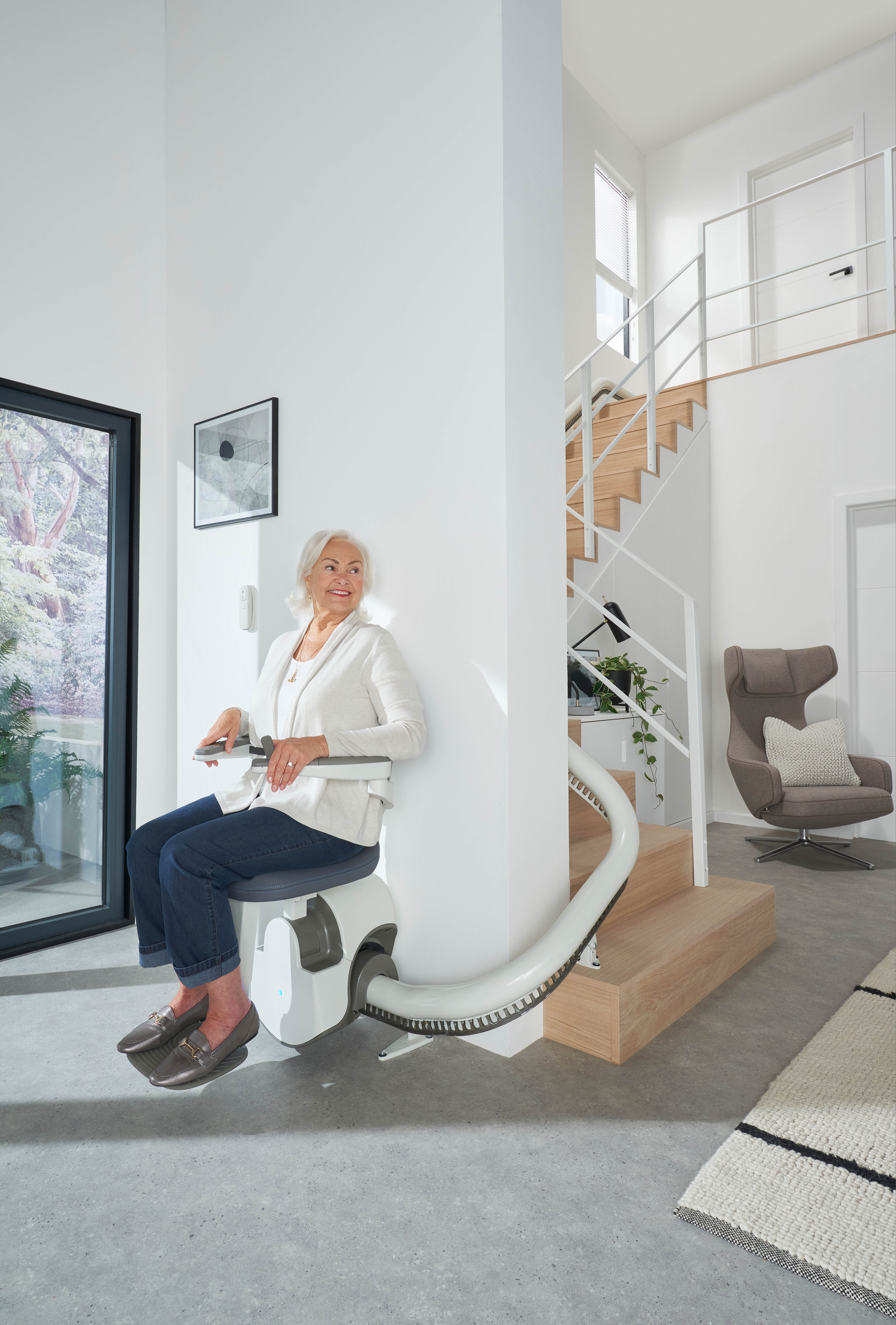 A woman riding an Access Flow X stairlift on a curved white rail through the open ground floor of a modern home