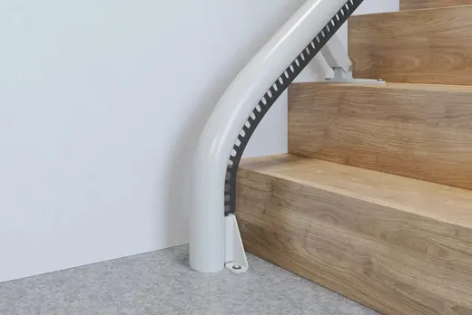 Close-up of the Access Flow X drop nose rail curving down to the floor at the bottom step of a wooden staircase