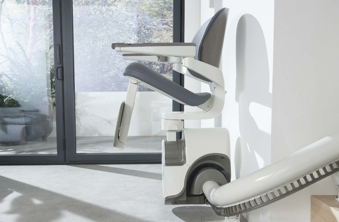 An Access Flow X folded away at the foot of a staircase beside a window, seat and footrest raised