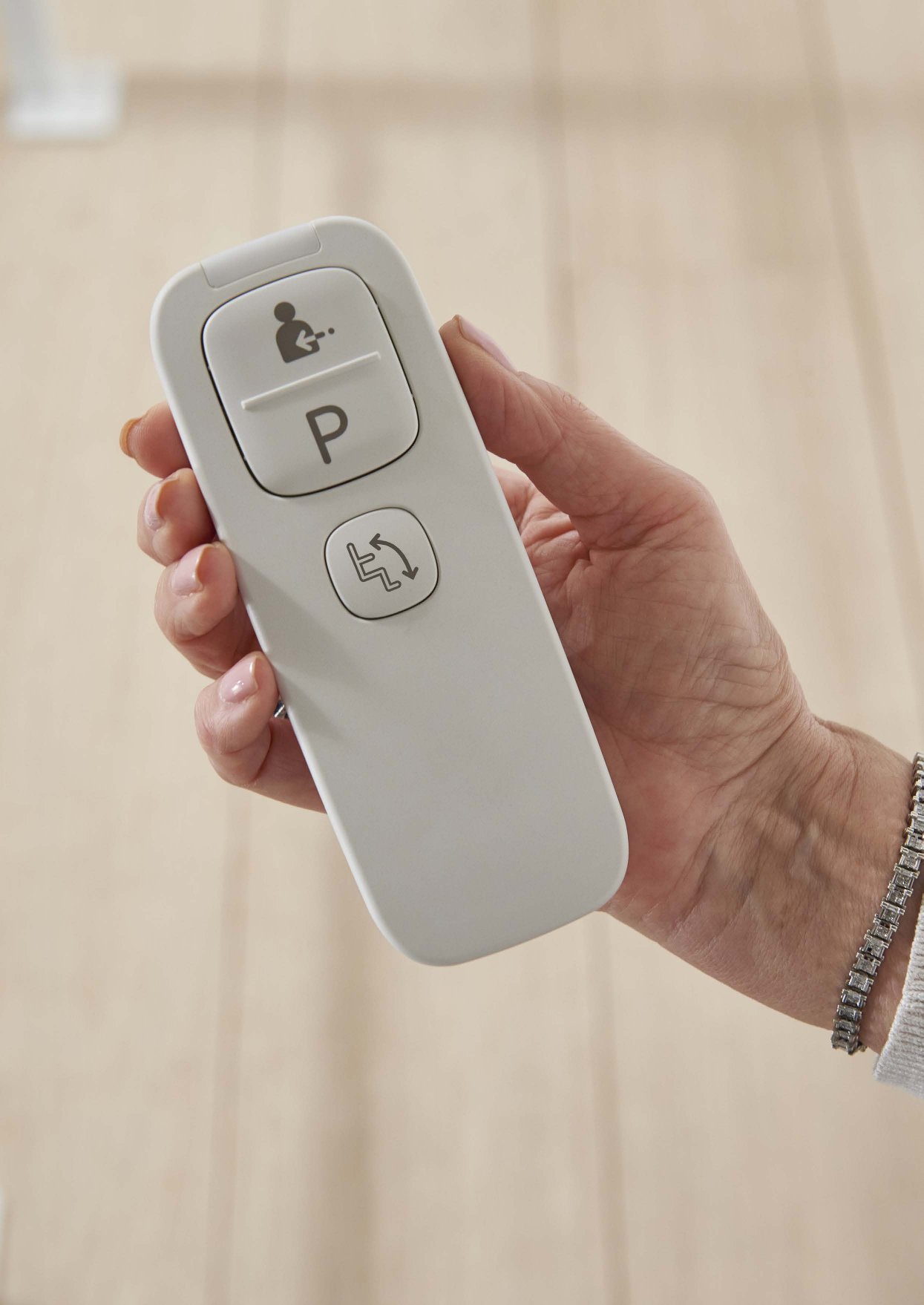 A hand holding the Access Flow X remote control, showing the call and park buttons and the status indicator