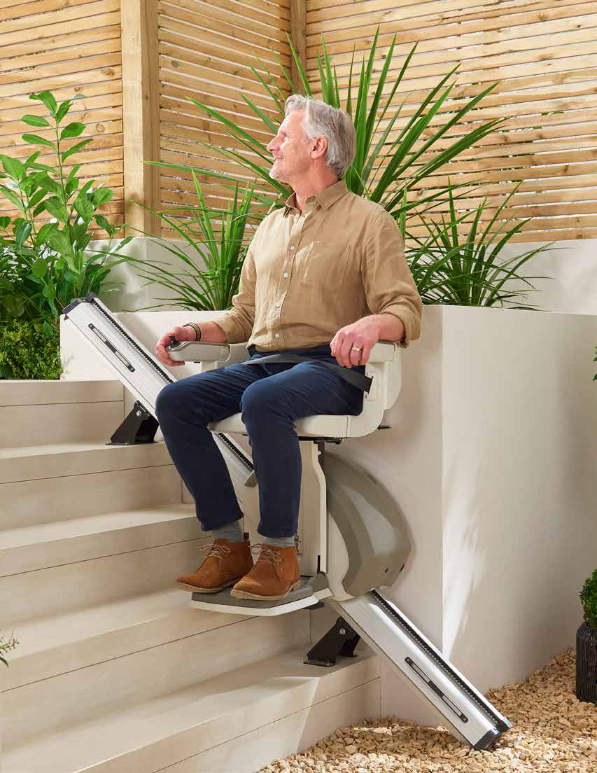 A man riding the Access HomeGlide Outdoor stairlift up a set of garden steps beside planted borders