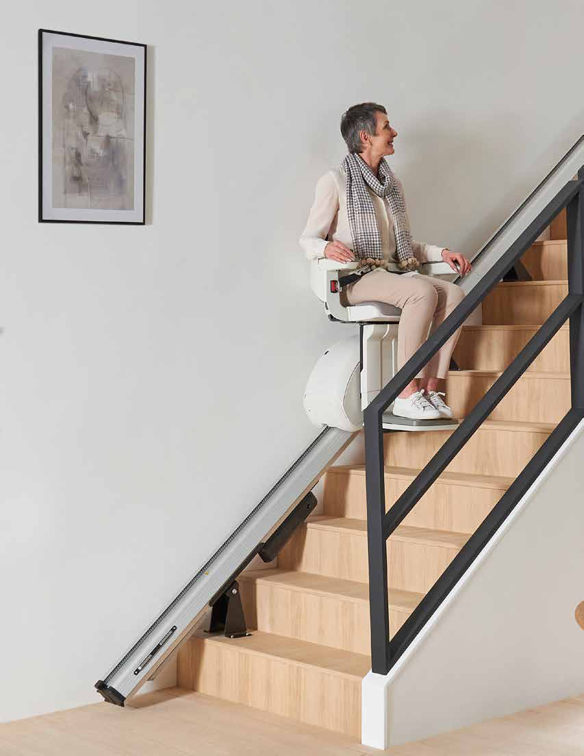 A woman riding the Access HomeGlide stairlift up a wooden staircase with a black metal balustrade
