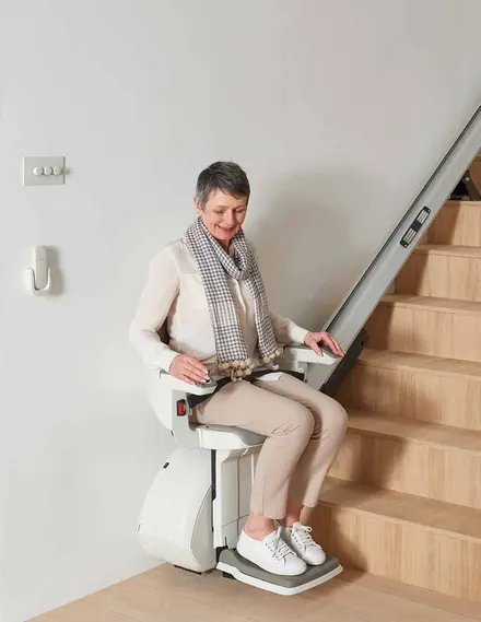 Mid-travel on a wooden staircase, with the wall-mounted remote visible at the top of the flight.
