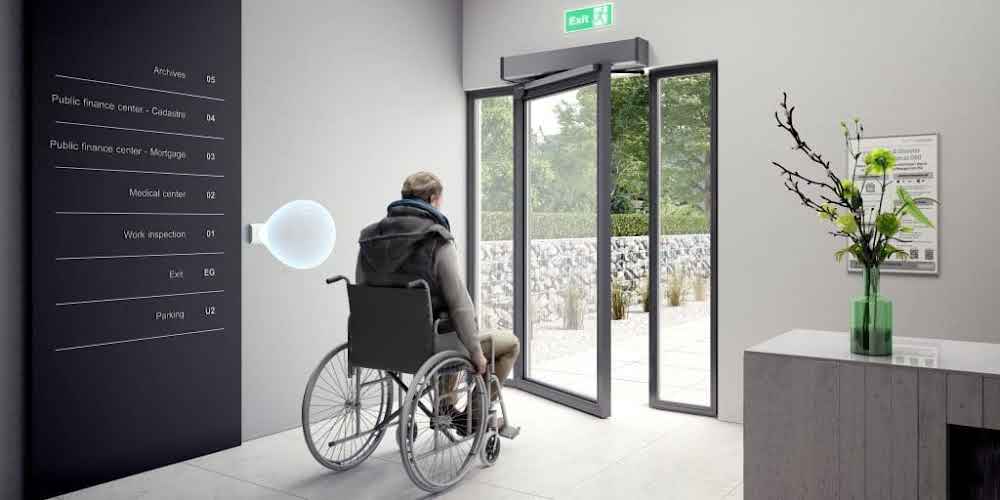 Wheelchair user approaching an entrance with an automatic door operator mounted above the door