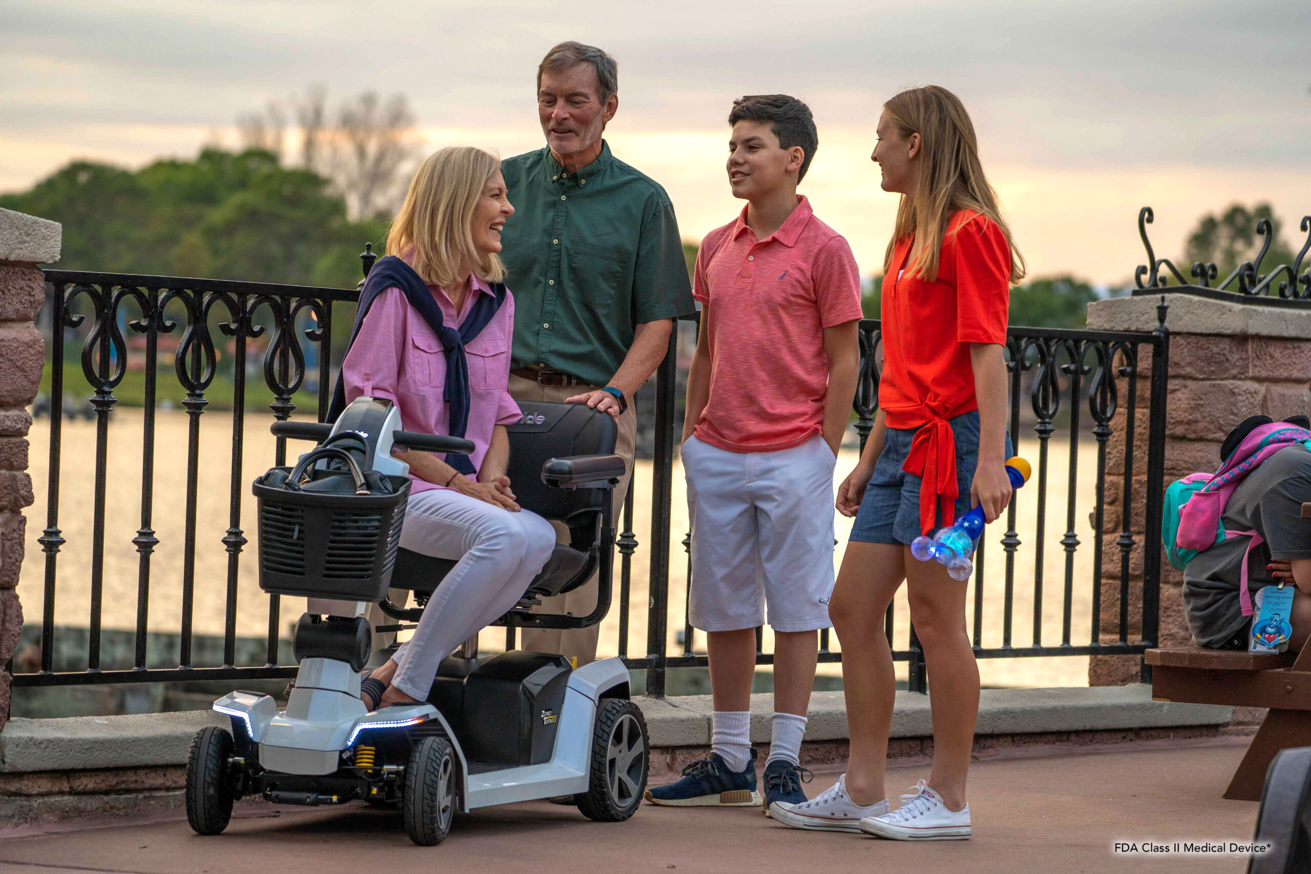 A woman on a mobility scooter talking with family beside a waterfront railing