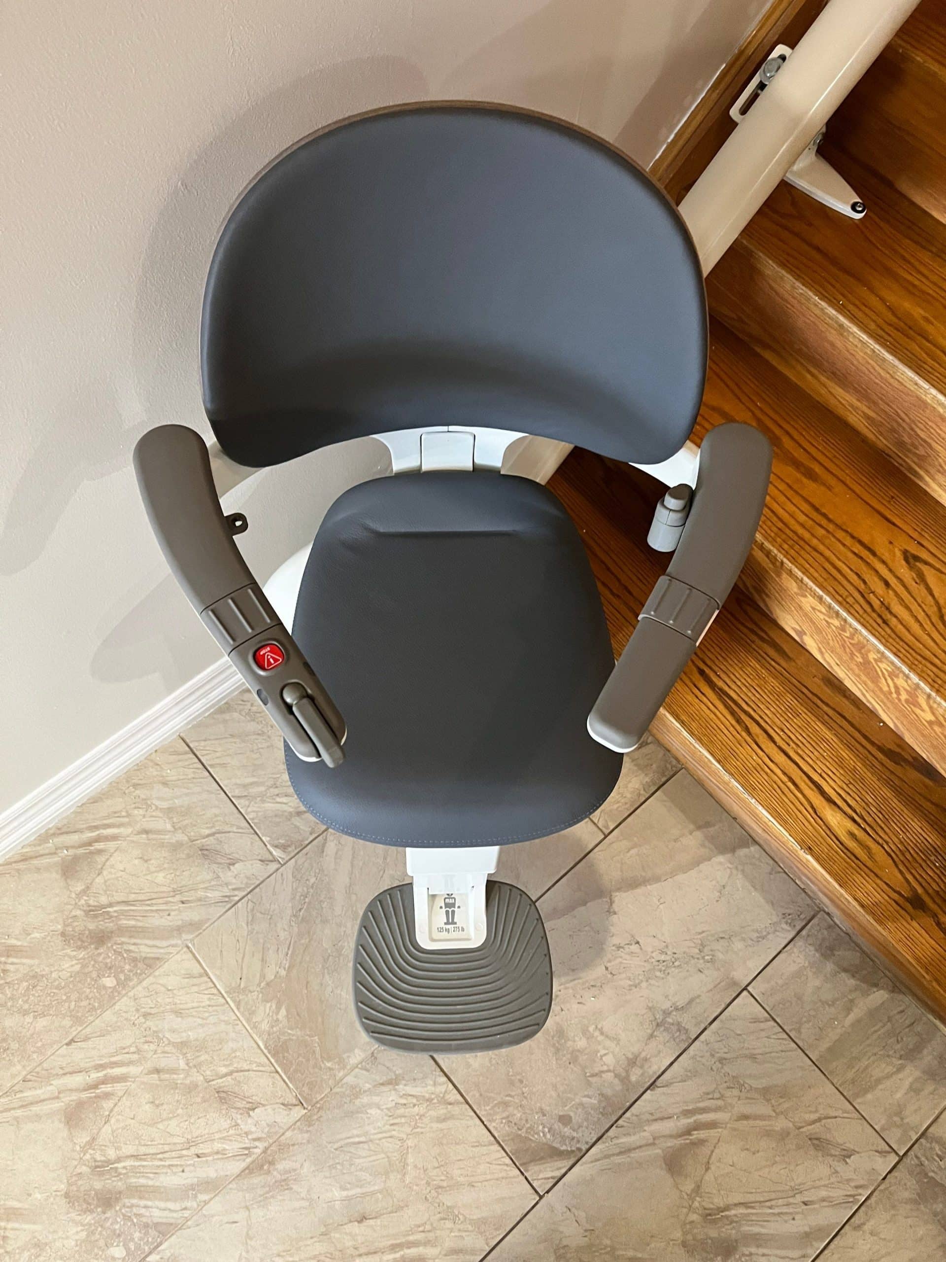 A grey curved stairlift chair parked at the bottom of a wood indoor stair
