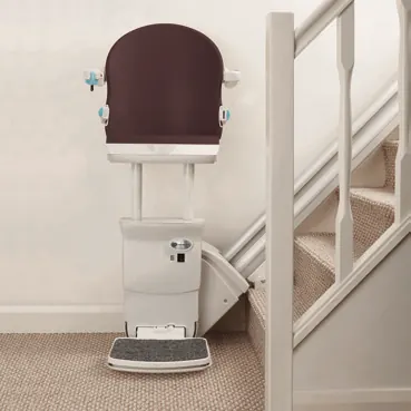 Handicare 1000 stairlift in Cacao upholstery folded at the foot of a white-spindled staircase