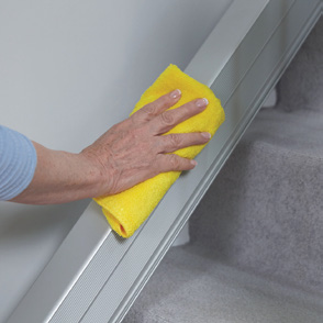 A hand wiping the Handicare 1100 rail clean with a yellow cloth