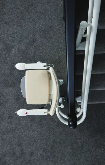 Overhead view of a Handicare stairlift chair folded and parked clear of a staircase on dark carpet