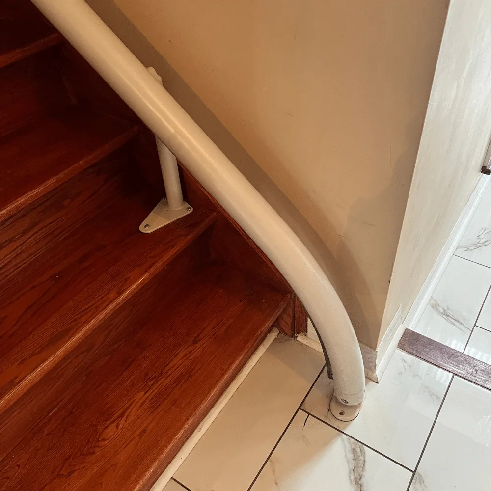 Drop nose rail end curving down to the tiled floor at the bottom step of a staircase