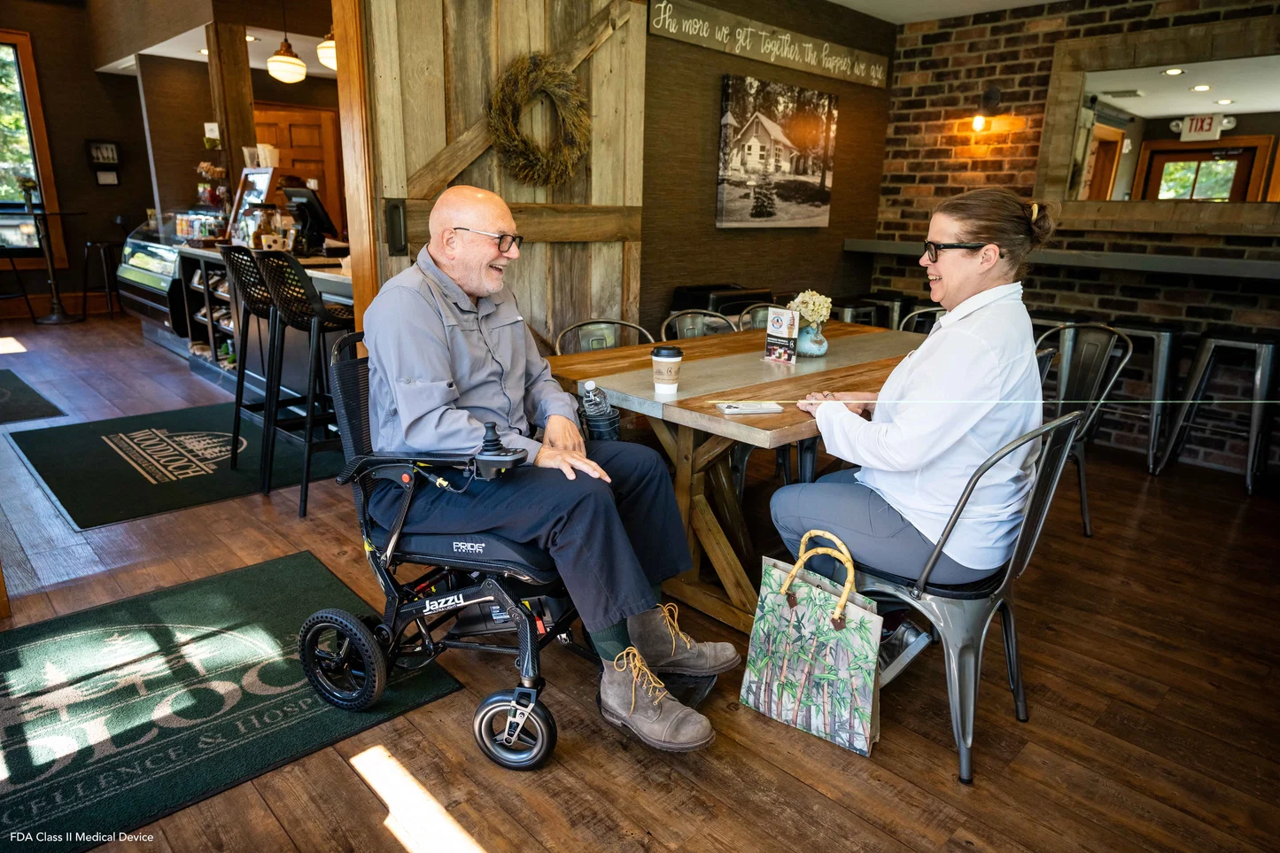 A man in a folding power wheelchair talking with a woman at a cafe table