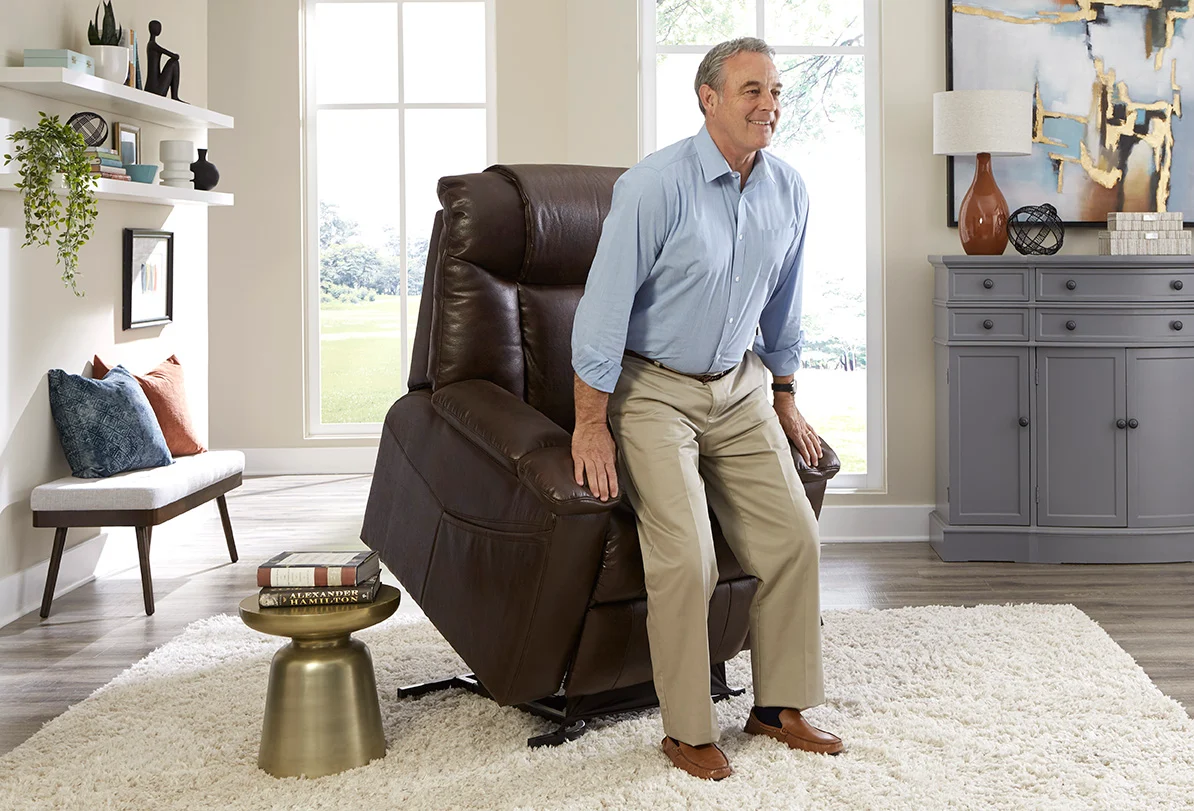 A man standing up from a brown lift chair in a furnished living room