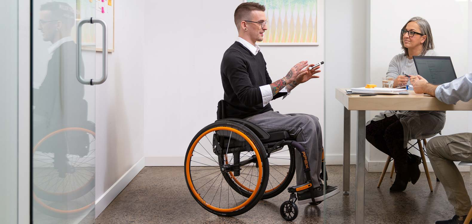 A man in a rigid manual wheelchair at a meeting table