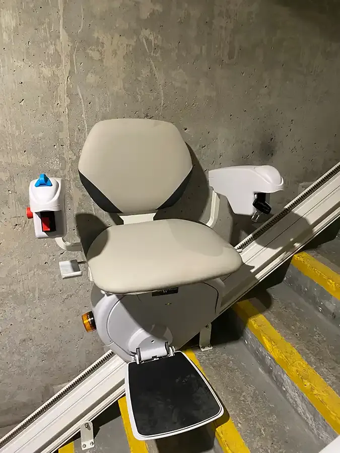 A Savaria K2 Plus parked on a concrete stairwell in a commercial building, beside treads with painted safety edges