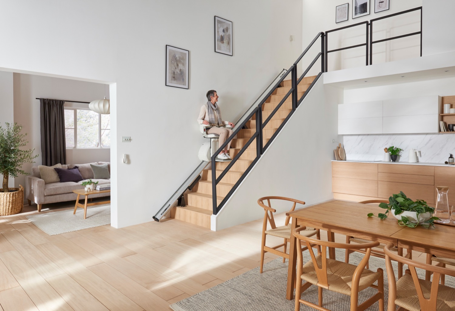 A woman riding a stairlift up a straight staircase in a bright home