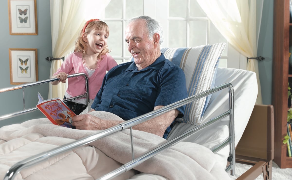A grandfather and grandchild sharing a book in a homecare bed